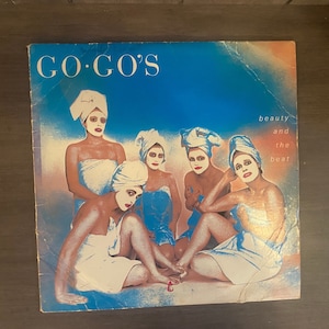 May include: A vintage vinyl record album cover featuring a group of five women in white towels, with the band name "GO-GO'S" and the album title "beauty and the beat" printed on the front.
