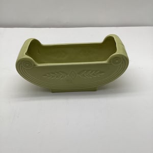 May include: A pale green ceramic planter shaped like a cradle with a decorative leaf design.
