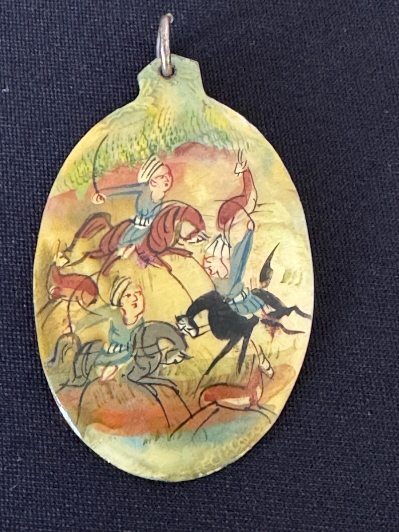 May include: An oval-shaped pendant with a hand-painted scene of three figures on horseback riding through a landscape. The figures are painted in shades of blue, red, and yellow, and the background is a mix of green and brown.
