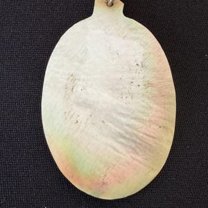 May include: A white oval pendant with a silver loop at the top. The pendant has a slightly iridescent sheen and is made of a smooth, polished material.