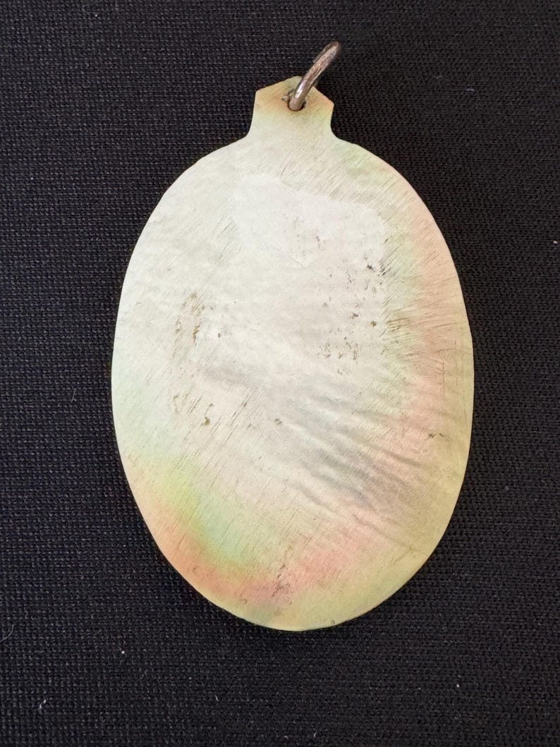 May include: A white oval pendant with a silver loop at the top. The pendant has a slightly iridescent sheen and is made of a smooth, polished material.