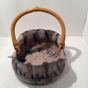 May include: A ceramic basket with a ruffled rim and a brown wooden handle. The basket is decorated with blue and purple glaze.