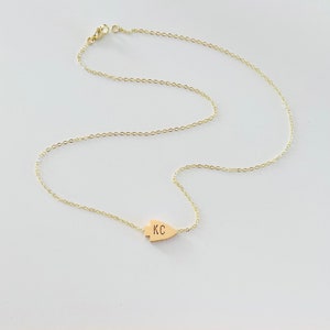 May include: A gold chain necklace with a gold arrowhead pendant. The pendant has the initials "KC" engraved on it.