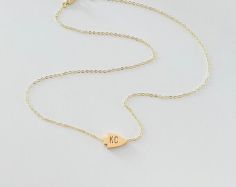 Op de afbeelding: Een gouden ketting met een gouden pijlpunt hanger. De hanger heeft de initialen "KC" gegraveerd.