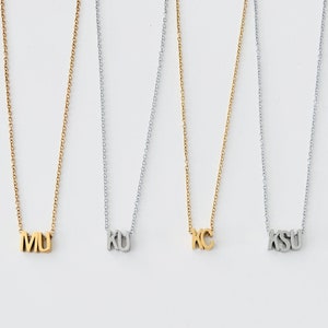 May include: Four gold and silver necklaces with initial pendants. The necklaces spell out "MU", "KU", "KC", and "KSU".