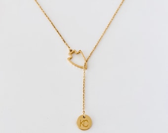May include: A gold necklace with a delicate chain and a pendant shaped like a mountain with a small circle pendant that says "KC" hanging from it.