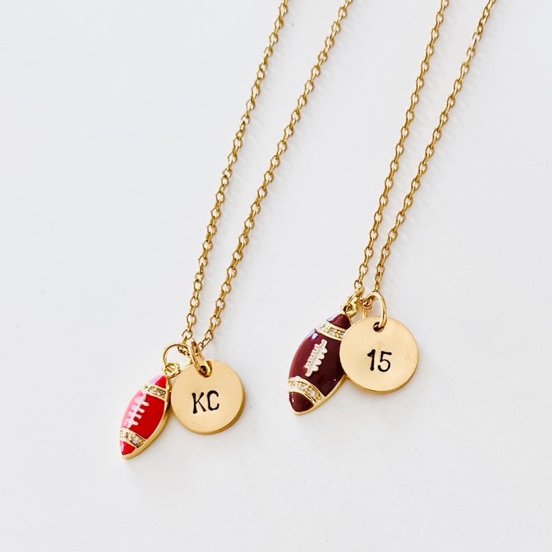 May include: Two gold necklaces with football charms. One necklace has a charm with the initials "KC" and the other has a charm with the number "15".