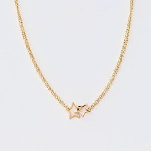 May include: A gold-colored necklace featuring two connected star pendants. The necklace has a delicate chain design and is displayed against a white background. The stars are linked together, creating a simple yet elegant jewelry piece.