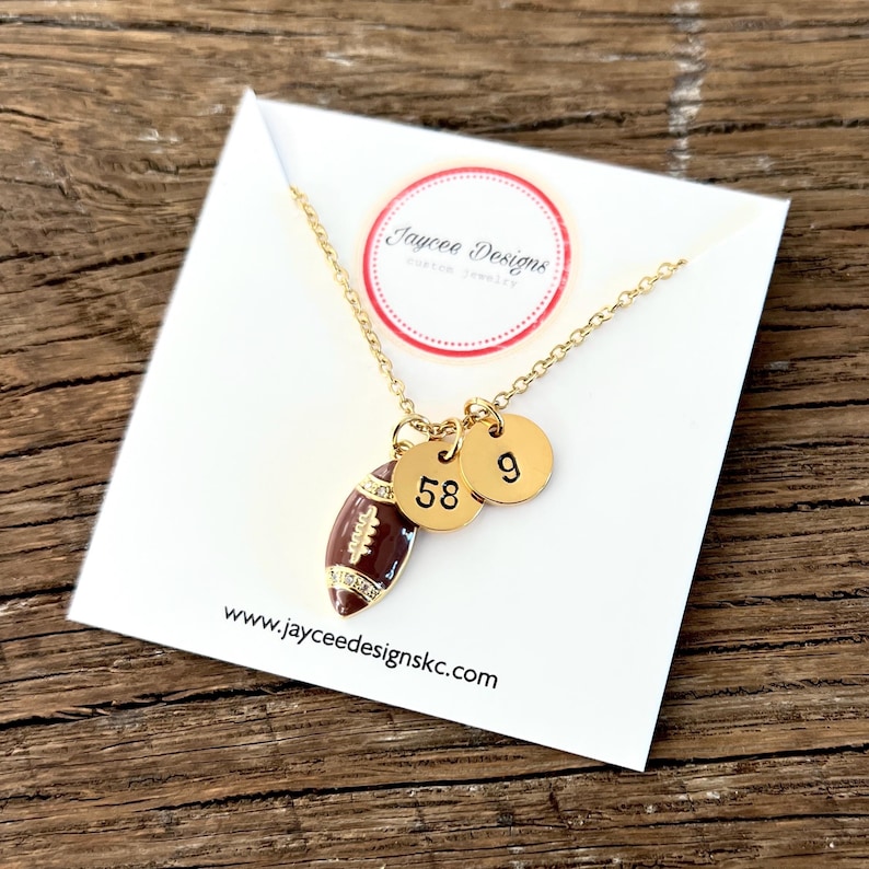 May include: Gold necklace with a brown football charm and two gold discs with the numbers 58 and 9. The necklace is on a white card with the text "Jaycee Designs" and "www.jaycee designskc.com".
