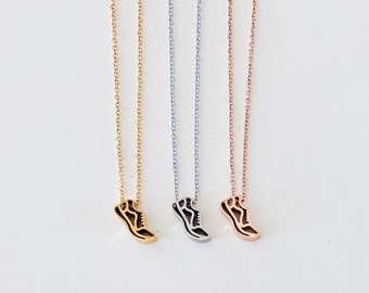May include: Three necklaces featuring running shoe pendants in gold, silver, and rose gold. Each pendant has a black outline. The fine chains match the pendant colour. The necklaces are presented against a white backdrop.