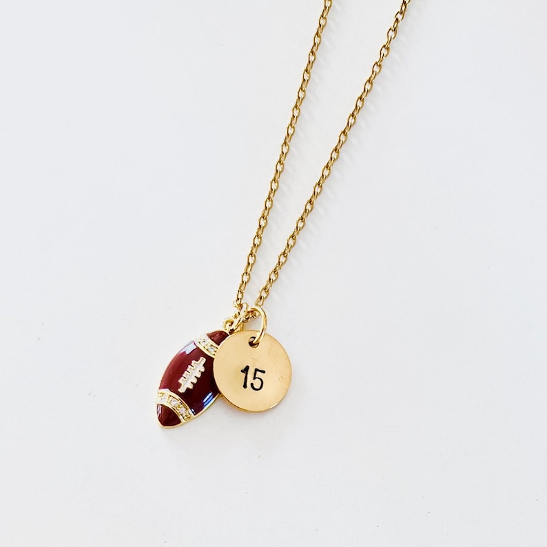 May include: Gold chain necklace with a brown football charm and a gold disc charm with the number 15.