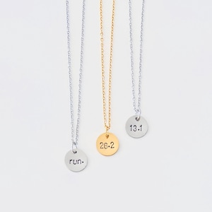 May include: Three silver necklaces with different pendants. The pendants are round and have the following text: "run.", "26.2", and "13.1".