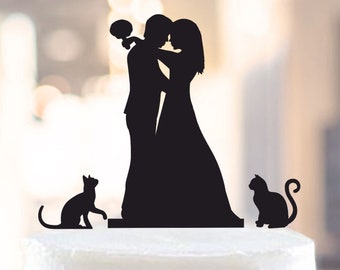May include: Black silhouette cake topper of a bride and groom embracing, with two black cats on either side.