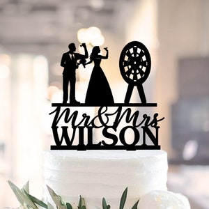 May include: Black silhouette cake topper featuring a bride and groom throwing darts at a dartboard with the text "Mr & Mrs Wilson" below.
