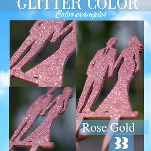 Op de afbeelding: Close-up van een paar glitter bruidstaarttoppers in roosgoud. Het paar houdt elkaars hand vast en de bruid draagt een jurk met een zwierige rok. De tekst "Rose Gold" is zichtbaar in de afbeelding.