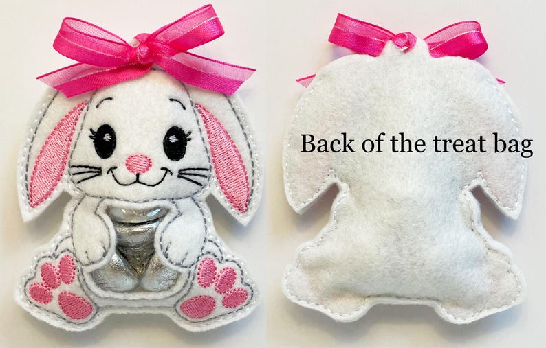 May include: A white felt bunny treat bag with pink ears, a pink bow, and a clear plastic window for holding treats. The back of the bag is plain white felt. "Back of the treat bag" is written on the back of the bag.