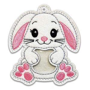 May include: White felt bunny with pink ears and paws. The bunny has a clear plastic window in the center of its body.