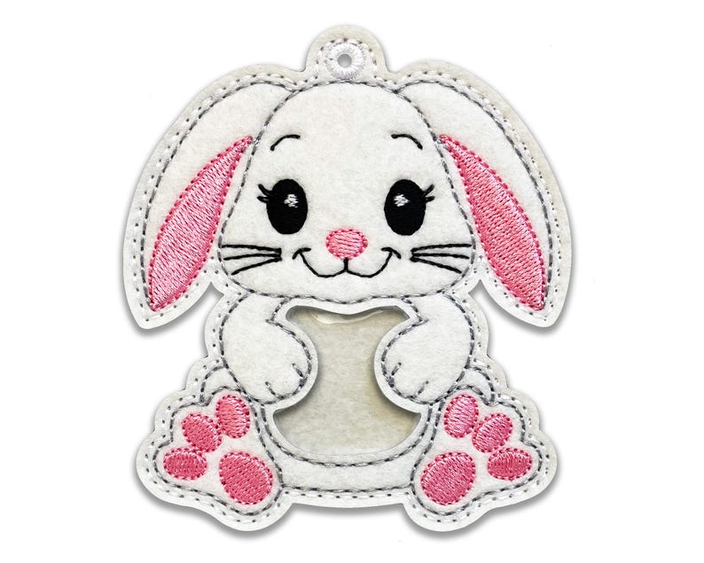 May include: White felt bunny with pink ears and paws. The bunny has a clear plastic window in the center of its body.