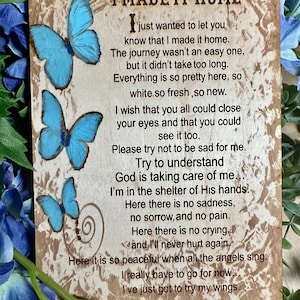 May include: A rustic wooden sign with a poem about finding peace and comfort after a difficult journey. The poem is written in a handwritten font and features blue butterflies. The sign reads "I made it home. I just wanted to let you know that I made it home. The journey wasn't an easy one, but it didn't take too long. Everything is so pretty here, so white.so fresh, so new. I wish that you all could close your eyes and that you could see it too. Please try not to be sad for me. Try to understand God is taking care of me. I'm in the shelter of His hands. Here there is no sadness, no sorrow, and no pain. Here there is no crying, and I'll never hurt again. Here it is so peaceful when all the angels sing. I really have to go for now. I've just got to try my wings."