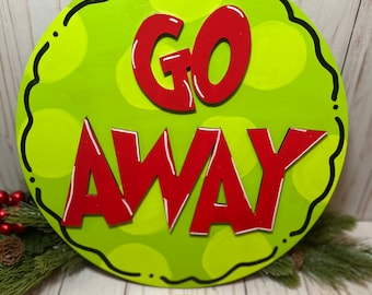 May include: A round green and red wooden sign with the words "GO AWAY" in red letters. The sign has a scalloped edge and a polka dot pattern.