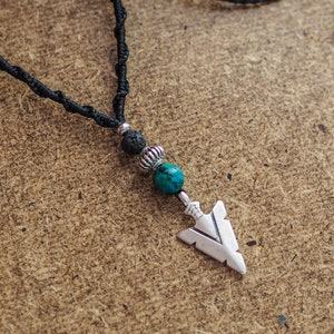 Può includere: Una collana con cordoncino nero con un ciondolo a forma di freccia d'argento, una perla di turchese e una di lava.