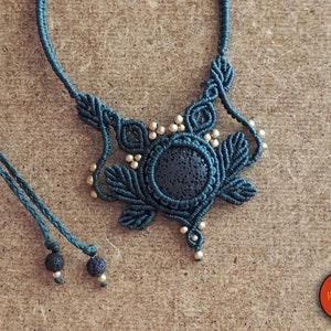 May include: A dark green macrame necklace with a round lava rock pendant and gold beads. The necklace has a tassel at the end.