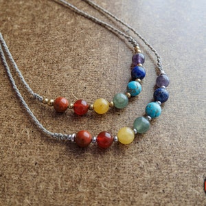 Può includere: Una collana a doppio filo con sette pietre chakra nei colori dell'arcobaleno, tra cui rosso, arancione, giallo, verde, blu, indaco e viola. La collana è realizzata con un cordoncino grigio e perline argentate.