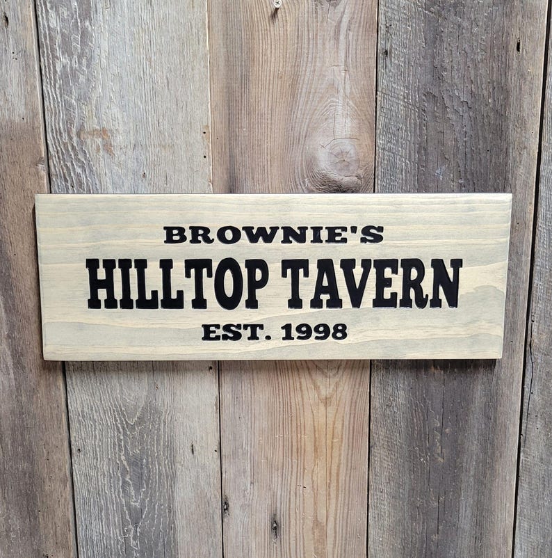 This hand carved wooden sign features a family name and the name of their tavern or bar. with an Est date. you choose our most popular wording of Man Cave, Tavern, Home Bar or you can write your own up to 6 total words, 2 words per line and up to 3 lines. you get your choice of stain color. the hand carved wording is carved then painted in black with black border trim. the Photo'd sign is displayed on an old weather barn wood backdrop.