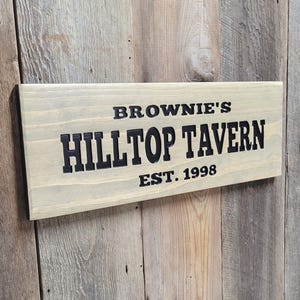 This hand carved wooden sign features a family name and the name of their tavern or bar. with an Est date. you choose our most popular wording of Man Cave, Tavern, Home Bar or you can write your own up to 6 total words, 2 words per line and up to 3 lines. you get your choice of stain color. the hand carved wording is carved then painted in black with black border trim. the Photo'd sign is displayed on an old weather barn wood backdrop.