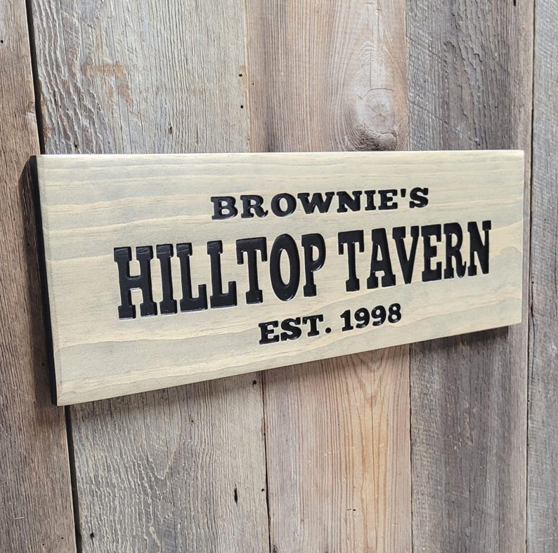 This hand carved wooden sign features a family name and the name of their tavern or bar. with an Est date. you choose our most popular wording of Man Cave, Tavern, Home Bar or you can write your own up to 6 total words, 2 words per line and up to 3 lines. you get your choice of stain color. the hand carved wording is carved then painted in black with black border trim. the Photo'd sign is displayed on an old weather barn wood backdrop.