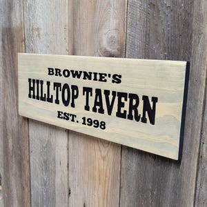 This hand carved wooden sign features a family name and the name of their tavern or bar. with an Est date. you choose our most popular wording of Man Cave, Tavern, Home Bar or you can write your own up to 6 total words, 2 words per line and up to 3 lines. you get your choice of stain color. the hand carved wording is carved then painted in black with black border trim. the Photo'd sign is displayed on an old weather barn wood backdrop.