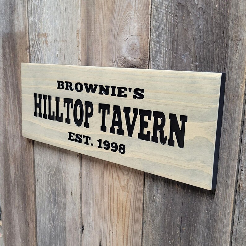 This hand carved wooden sign features a family name and the name of their tavern or bar. with an Est date. you choose our most popular wording of Man Cave, Tavern, Home Bar or you can write your own up to 6 total words, 2 words per line and up to 3 lines. you get your choice of stain color. the hand carved wording is carved then painted in black with black border trim. the Photo'd sign is displayed on an old weather barn wood backdrop.