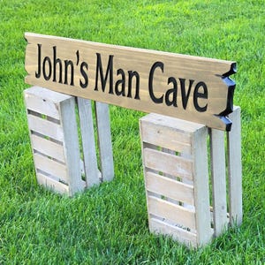 This is a hand carved wooden sign that is custom personalized to your first or last name and says man cave. can be personalized up to 5 words. the wording is carved and painted in black with a broken board effect on both ends on a stained background of your choice from the drop-down menu.