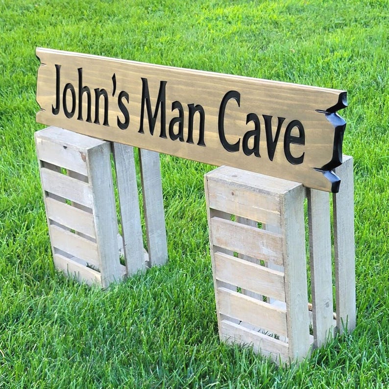 This is a hand carved wooden sign that is custom personalized to your first or last name and says man cave. can be personalized up to 5 words. the wording is carved and painted in black with a broken board effect on both ends on a stained background of your choice from the drop-down menu.