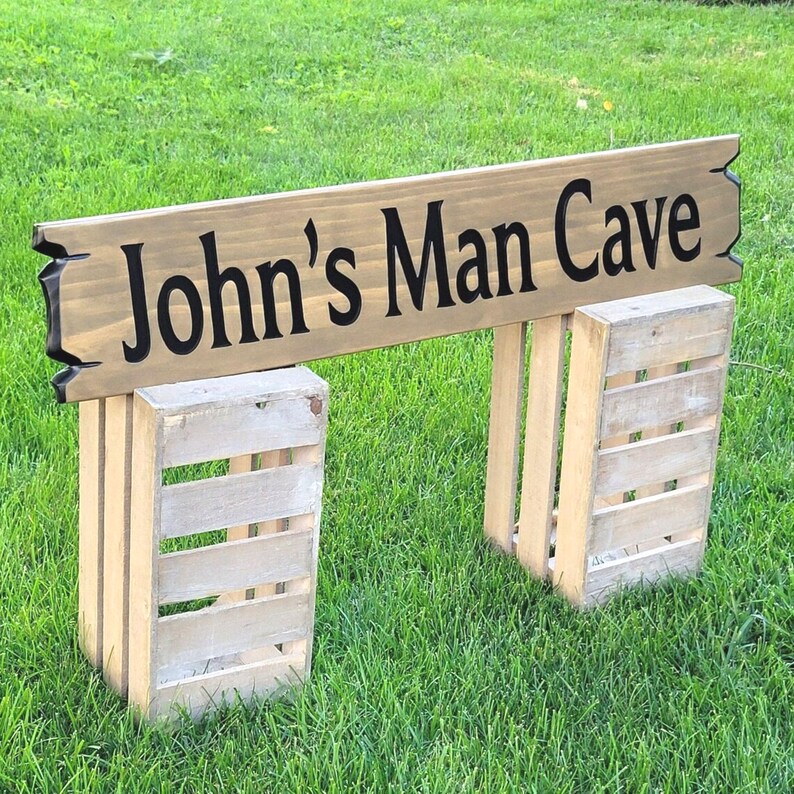 This is a hand carved wooden sign that is custom personalized to your first or last name and says man cave. can be personalized up to 5 words. the wording is carved and painted in black with a broken board effect on both ends on a stained background of your choice from the drop-down menu.