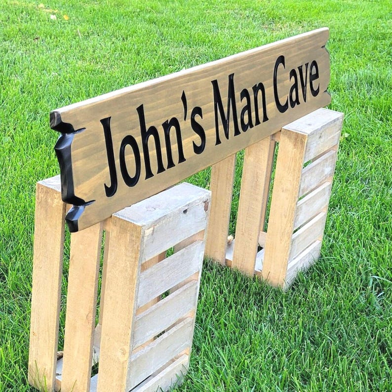 This is a hand carved wooden sign that is custom personalized to your first or last name and says man cave. can be personalized up to 5 words. the wording is carved and painted in black with a broken board effect on both ends on a stained background of your choice from the drop-down menu.
