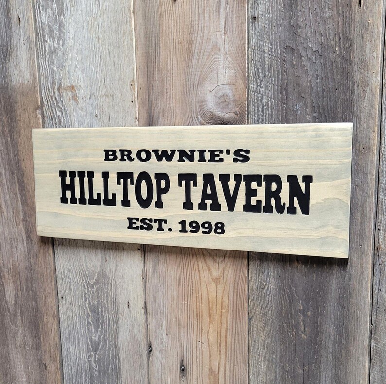 This hand carved wooden sign features a family name and the name of their tavern or bar. with an Est date. you choose our most popular wording of Man Cave, Tavern, Home Bar or you can write your own up to 6 total words, 2 words per line and up to 3 lines. you get your choice of stain color. the hand carved wording is carved then painted in black with black border trim. the Photo'd sign is displayed on an old weather barn wood backdrop.
