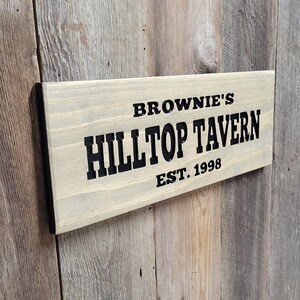 This hand carved wooden sign features a family name and the name of their tavern or bar. with an Est date. you choose our most popular wording of Man Cave, Tavern, Home Bar or you can write your own up to 6 total words, 2 words per line and up to 3 lines. you get your choice of stain color. the hand carved wording is carved then painted in black with black border trim. the Photo'd sign is displayed on an old weather barn wood backdrop.
