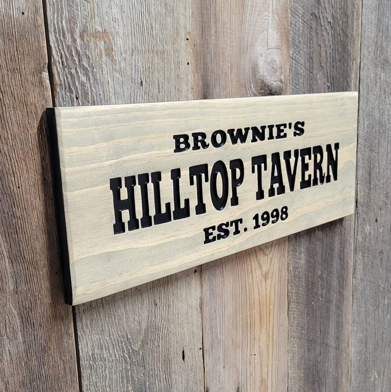 This hand carved wooden sign features a family name and the name of their tavern or bar. with an Est date. you choose our most popular wording of Man Cave, Tavern, Home Bar or you can write your own up to 6 total words, 2 words per line and up to 3 lines. you get your choice of stain color. the hand carved wording is carved then painted in black with black border trim. the Photo'd sign is displayed on an old weather barn wood backdrop.