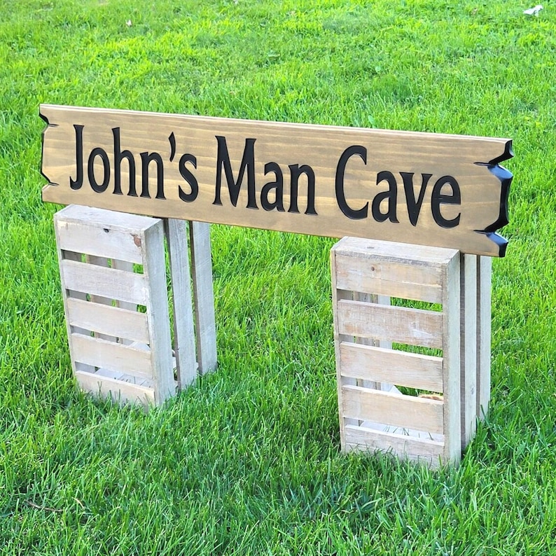 This is a hand carved wooden sign that is custom personalized to your first or last name and says man cave. can be personalized up to 5 words. the wording is carved and painted in black with a broken board effect on both ends on a stained background of your choice from the drop-down menu.