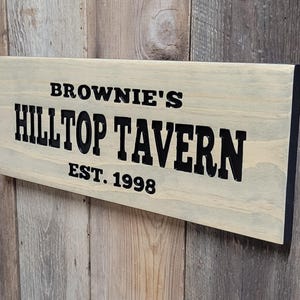 This hand carved wooden sign features a family name and the name of their tavern or bar. with an Est date. you choose our most popular wording of Man Cave, Tavern, Home Bar or you can write your own up to 6 total words, 2 words per line and up to 3 lines. you get your choice of stain color. the hand carved wording is carved then painted in black with black border trim. the Photo'd sign is displayed on an old weather barn wood backdrop.