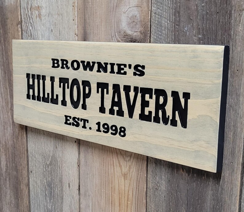 This hand carved wooden sign features a family name and the name of their tavern or bar. with an Est date. you choose our most popular wording of Man Cave, Tavern, Home Bar or you can write your own up to 6 total words, 2 words per line and up to 3 lines. you get your choice of stain color. the hand carved wording is carved then painted in black with black border trim. the Photo'd sign is displayed on an old weather barn wood backdrop.