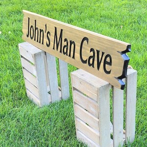 This is a hand carved wooden sign that is custom personalized to your first or last name and says man cave. can be personalized up to 5 words. the wording is carved and painted in black with a broken board effect on both ends on a stained background of your choice from the drop-down menu.