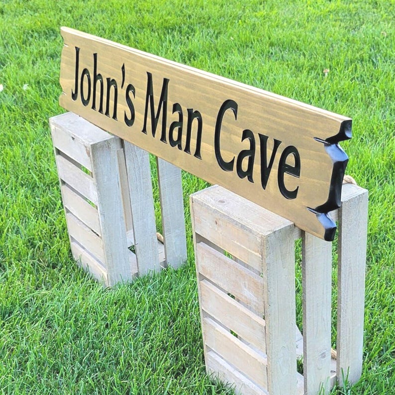 This is a hand carved wooden sign that is custom personalized to your first or last name and says man cave. can be personalized up to 5 words. the wording is carved and painted in black with a broken board effect on both ends on a stained background of your choice from the drop-down menu.
