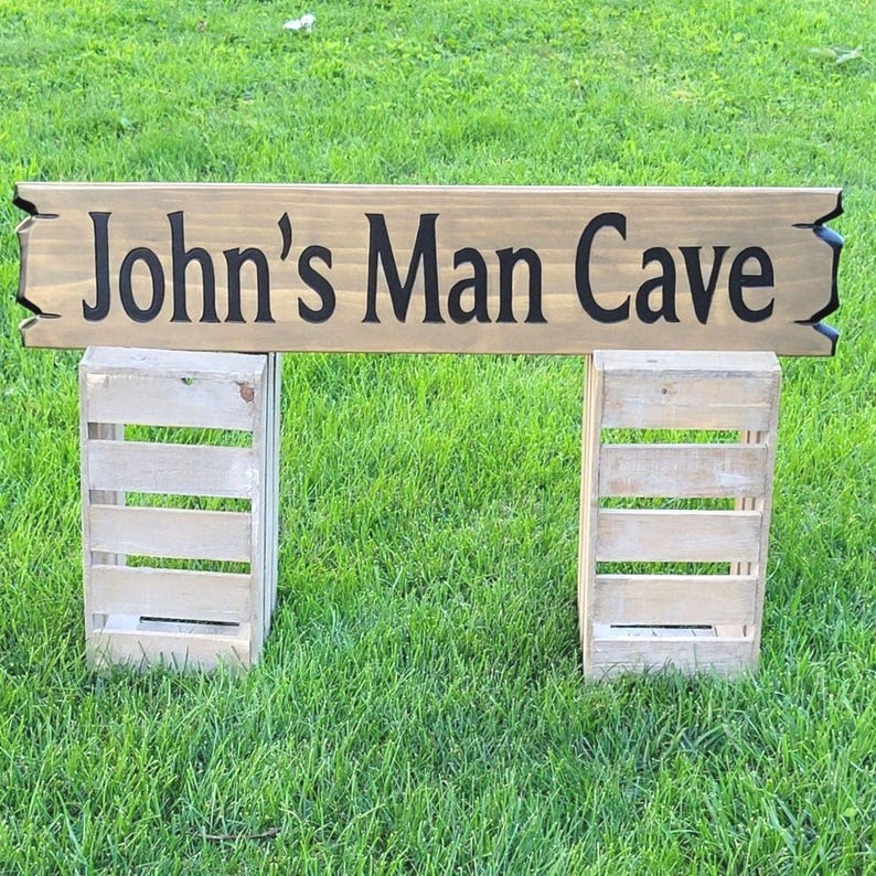 This is a hand carved wooden sign that is custom personalized to your first or last name and says man cave. can be personalized up to 5 words. the wording is carved and painted in black with a broken board effect on both ends on a stained background of your choice from the drop-down menu.
