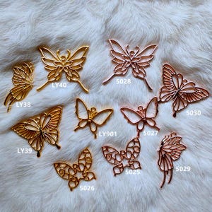 May include: Assortment of gold and rose gold butterfly charms with different designs and sizes. The charms are labeled with numbers and letters.