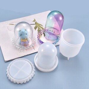 Peut inclure: Quatre moules en silicone transparent pour l'artisanat de la résine. Les moules sont en forme de dôme, de base ronde avec un dessus divisé et de cylindre haut avec trois pieds. Le moule en dôme est présenté avec un dôme en verre transparent avec une petite figurine à l'intérieur.