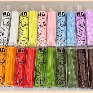 May include: A collection of 16 colorful bundles of thin, flexible, plastic straws. Each bundle is wrapped in clear plastic and features a cartoon dog and cat design with the text "特立" on the front.