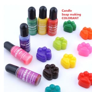 May include: Set of ten 12ml bottles of liquid soap making colourant in various colours, including pink, purple, green, yellow, orange, and red. The bottles have black caps and labels with the word "COLORANT" printed on them. The colourant is shown in small paw-shaped moulds.