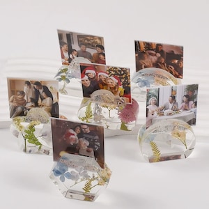 May include: Six clear resin photo holders with dried flowers and greenery inside. Each holder has a different photo of a family.